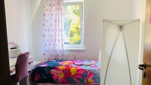 Ein Schlafzimmer mit Bett, Schreibtisch, Stuhl, Fenster mit Vorhängen und einer Tür.