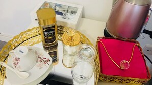 Ein Tablett mit einer Kaffeemaschine, einer Flasche Nescafe Gold, einem Teekessel, einem Glasbehälter und einer roten Schatulle mit Schmuck.