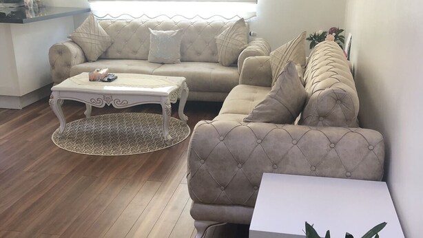 Ein modernes Wohnzimmer mit einem beigefarbenen Sofa, einem weißen Couchtisch und einer Topfpflanze.