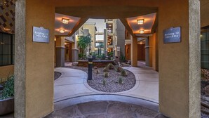 Eine Hotelhalle mit einer zentralen Sitzecke, zwei Hinweisschildern und einem gepflasterten Weg.