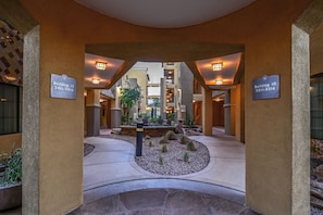 A hotel lobby with a central seating area, two building signs, and a stone pathway.