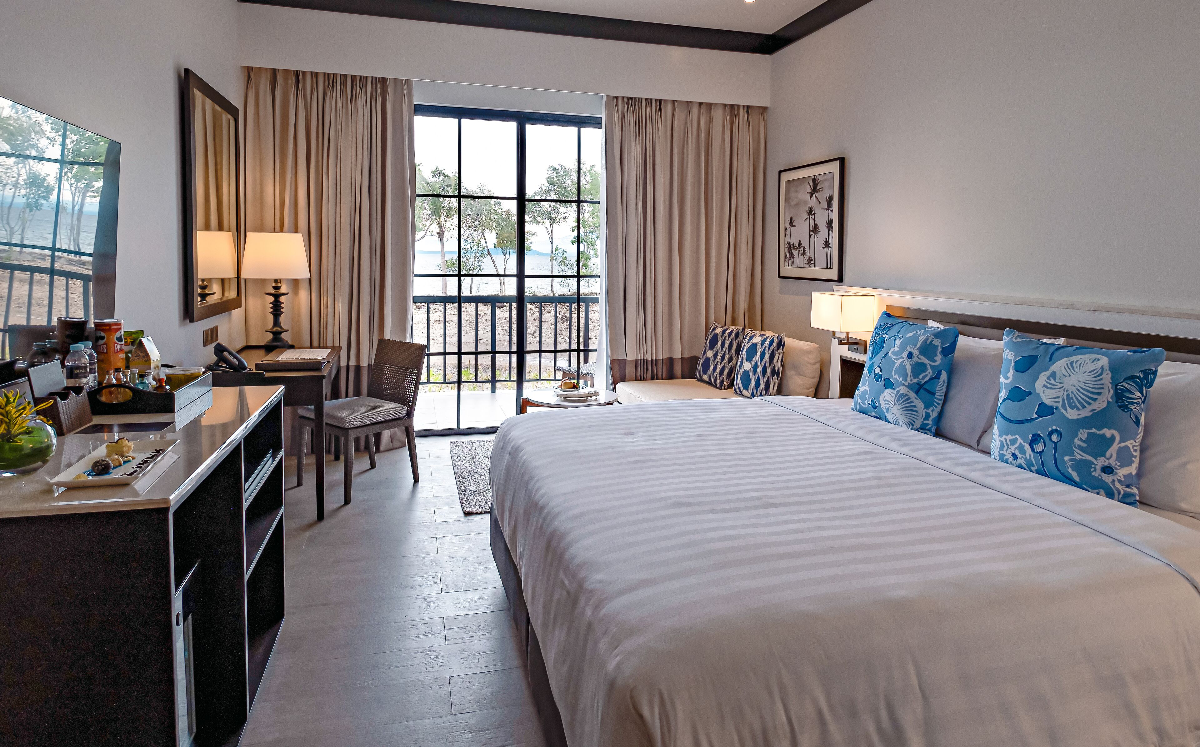 A hotel room with a bed, desk, chair, and a view of the beach.