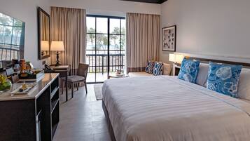 A hotel room with a bed, desk, chair, and a view of the beach.