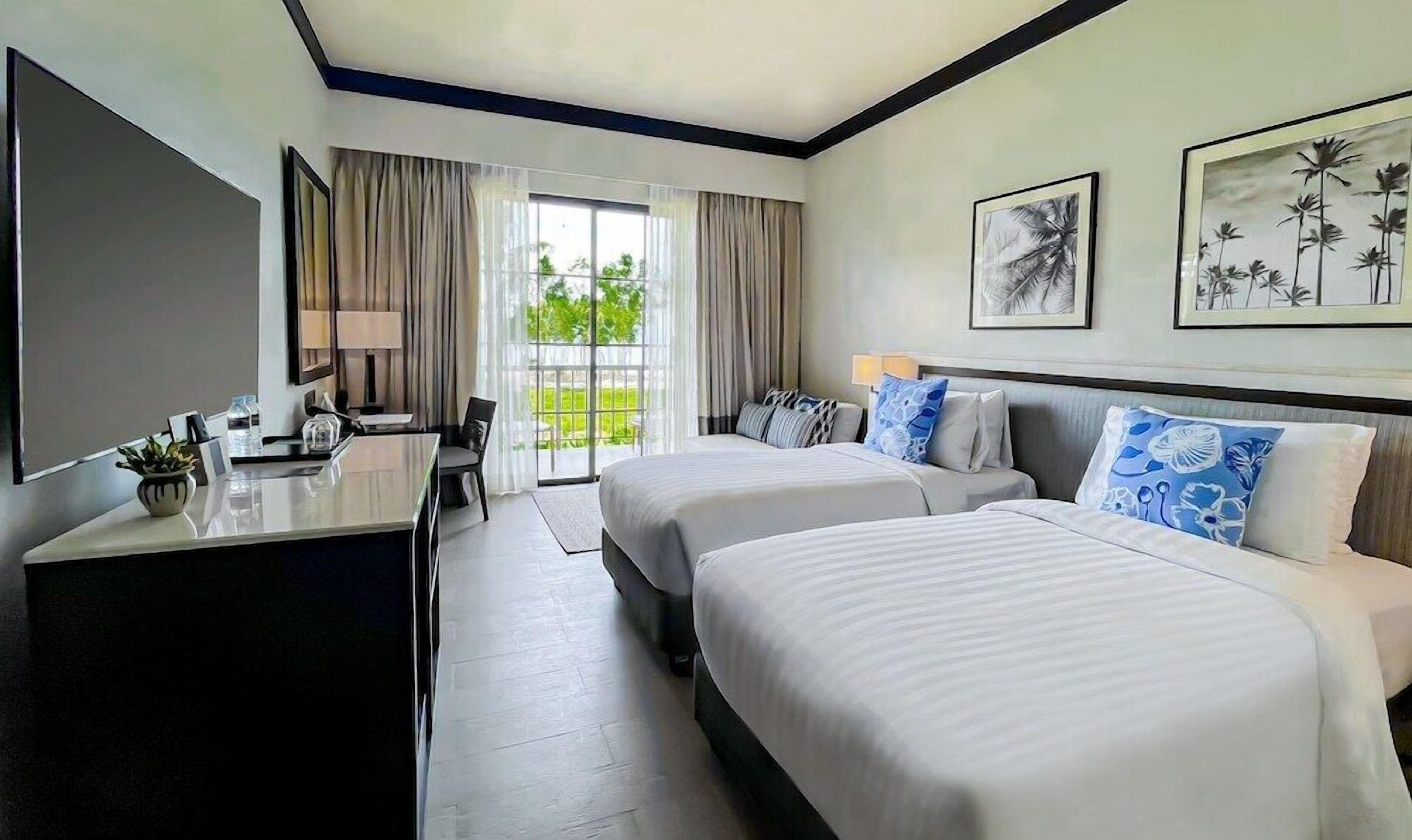 A hotel room with two beds, a desk, a chair, and a large window with curtains.