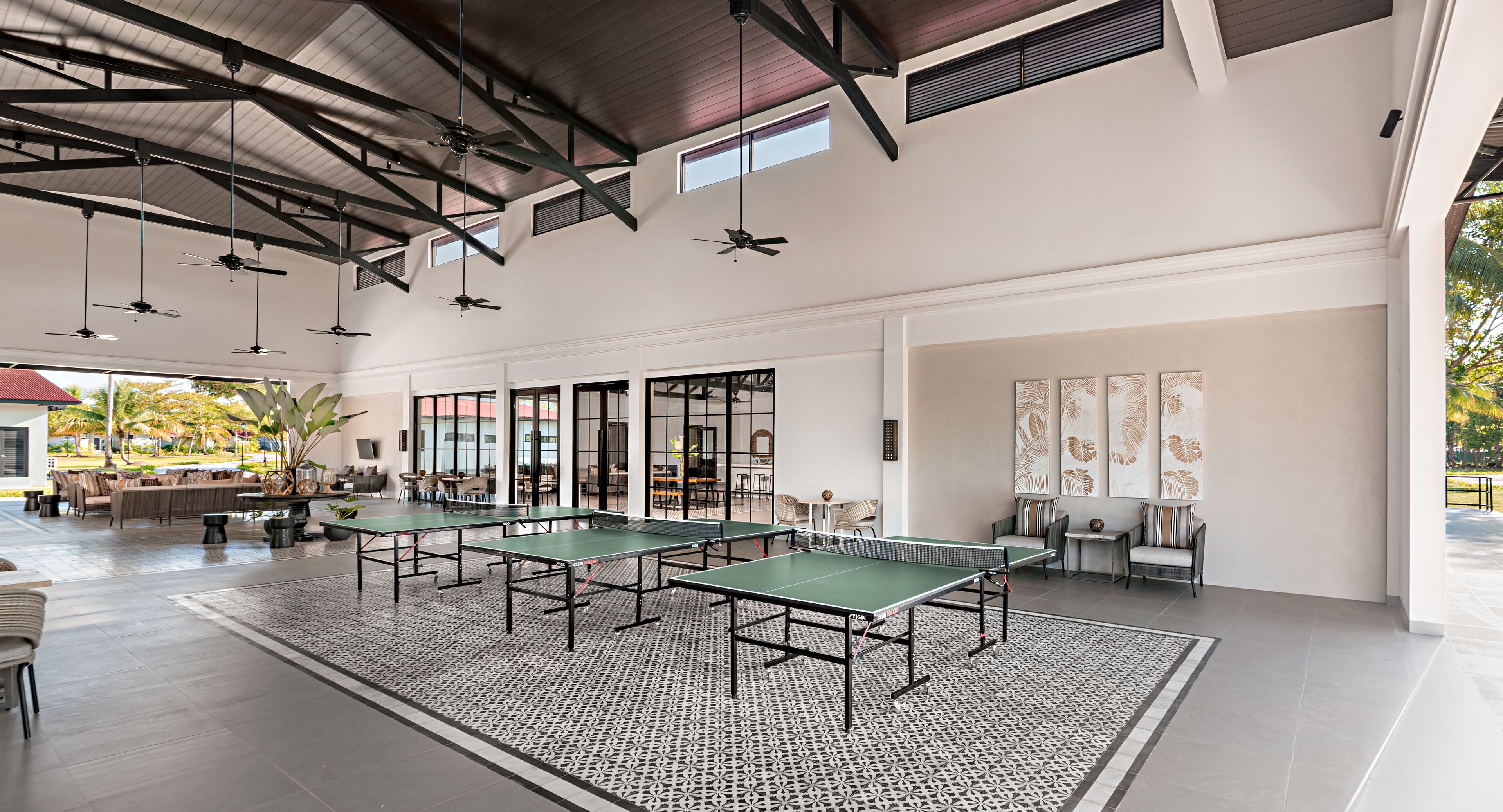 A spacious indoor area with multiple ping pong tables, ceiling fans, and a patterned floor.