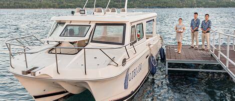 A boat docked at a pier with a forested shoreline in the background.