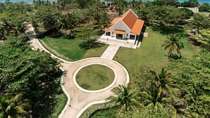 Une vue aérienne d’une propriété située sur la côte, avec un bâtiment blanc doté d’un toit rouge, entouré d’une végétation luxuriante et de palmiers, offrant une vue dégagée sur l’océan.