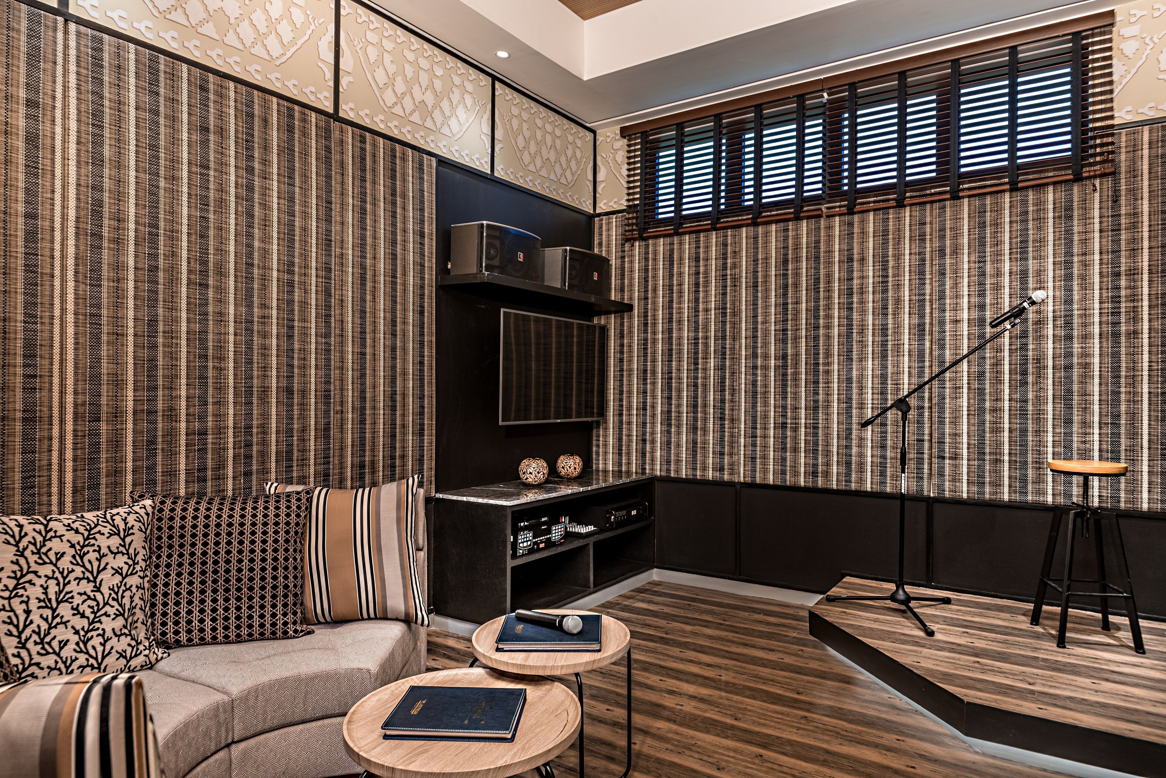 A modern living room with a curved sofa, a small wooden table, a black entertainment unit, and a large window with blinds.