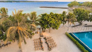 Un complexe hôtelier situé en bord de mer, doté d’une piscine, de palmiers et offrant une vue sur l’océan.