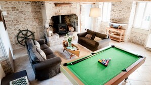 A cozy living room with a pool table, a fireplace, and a stone wall.