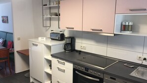 Een compacte keuken met witte kastjes, een inbouwoven, een koffiezetapparaat en een broodrooster.