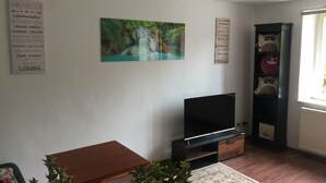 Een woonkamer met een flatscreen televisie, een boekenkast vol knuffels en een schilderij van een waterval.