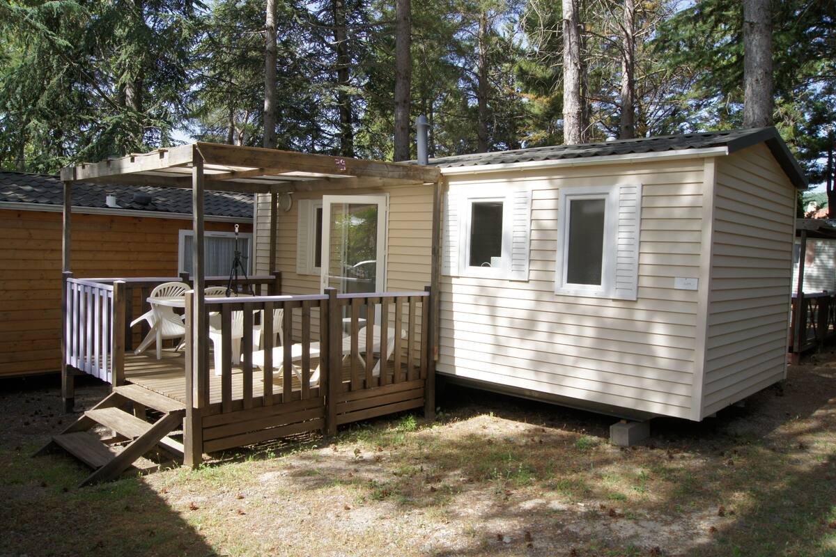 A mobile home with a deck and a small porch, surrounded by trees.
