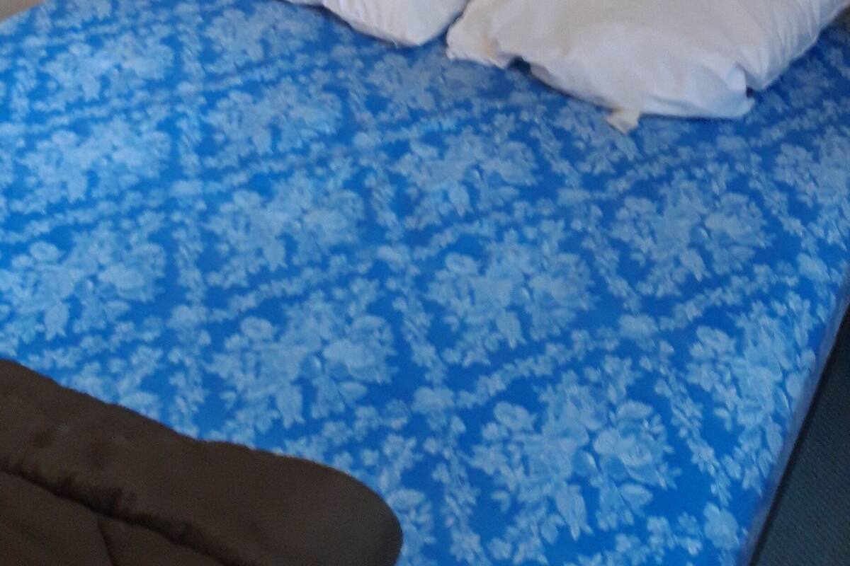 A single bed with a blue floral bedspread and two white pillows.