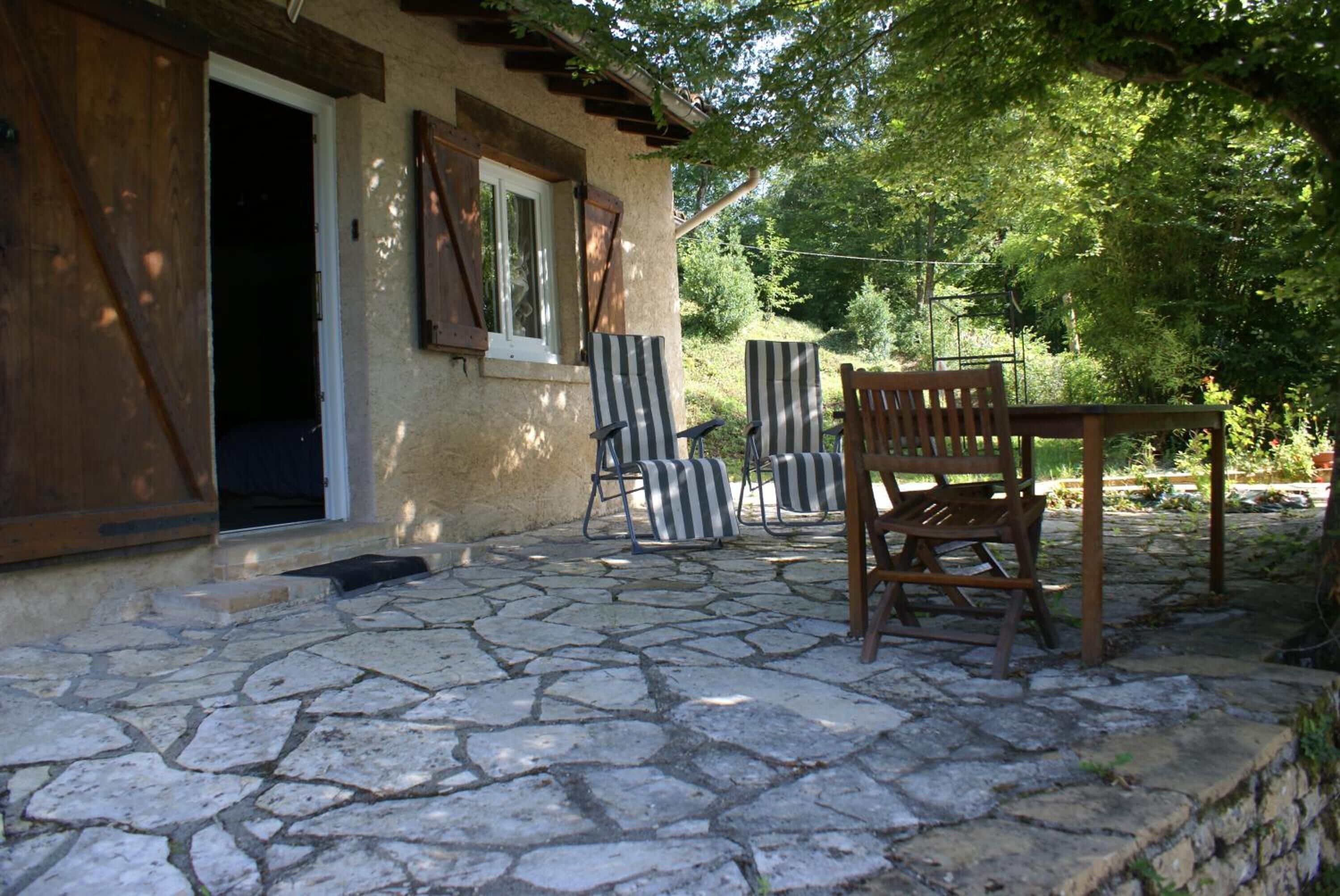Un patio con pavimento in pietra, un tavolo e sedie in legno, una panca di legno e una porta che dà su una stanza.