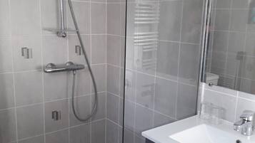Un baño moderno con cabina de ducha de vidrio, un lavabo blanco y un mueble oscuro.