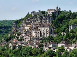 A historic town built on a rocky hill with a prominent castle-like structure. - Domisiladore (Latouille-Lentillac)