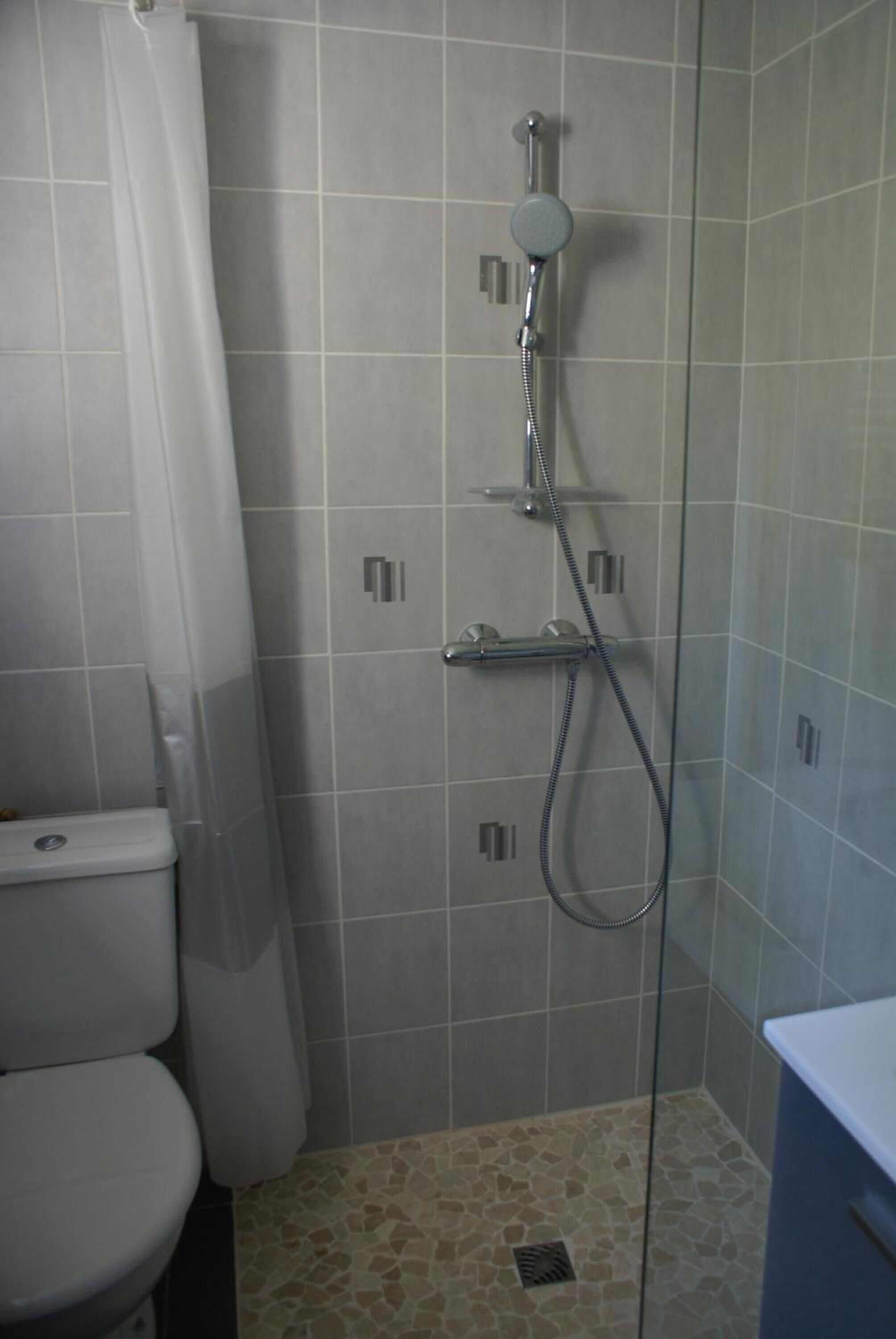 Ein kleines Badezimmer mit Fliesen, einer Dusche, einer Toilette und einem Waschbecken.