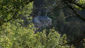 Un bâtiment historique en pierre, doté d’un toit en pente, entouré d’une forêt dense.