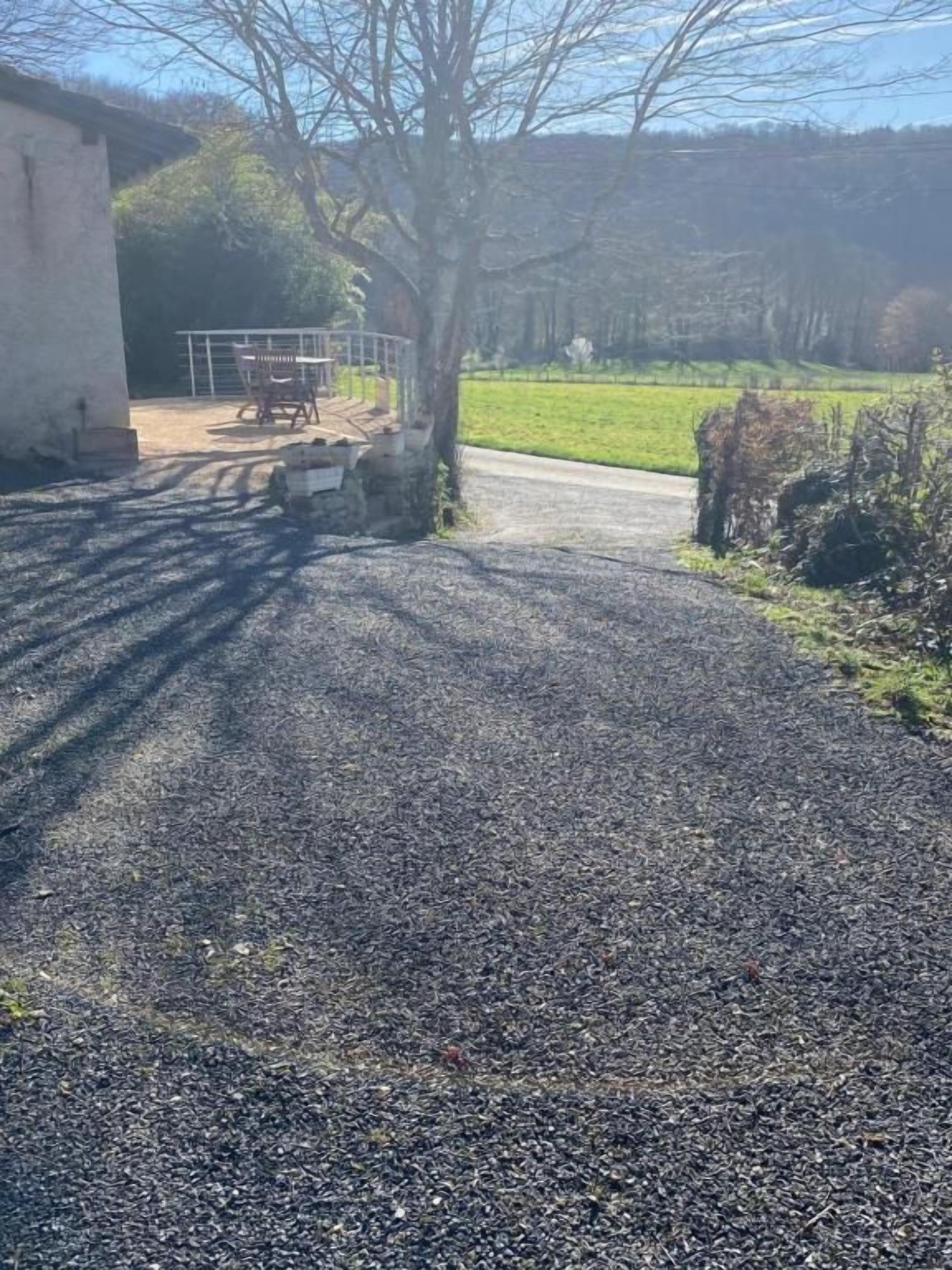 A gravel driveway leading to a building with a metal gate, surrounded by greenery and a clear sky.