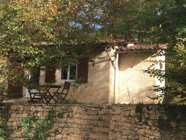 A rustic stone building with a tiled roof, a wooden table, and chairs outside. - Domisiladore (Latouille-Lentillac)