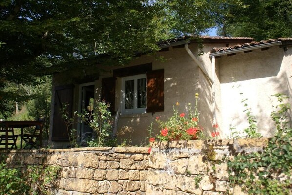 A rustic stone house with a wooden door and window shutters, surrounded by greenery and a stone wall. - Domisiladore (Latouille-Lentillac)