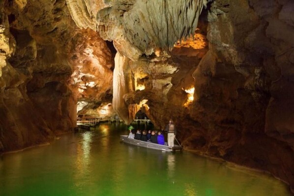 A boat tour inside a cave with stalactites and stalagmites, illuminated by artificial lighting. - Domisiladore (Latouille-Lentillac)