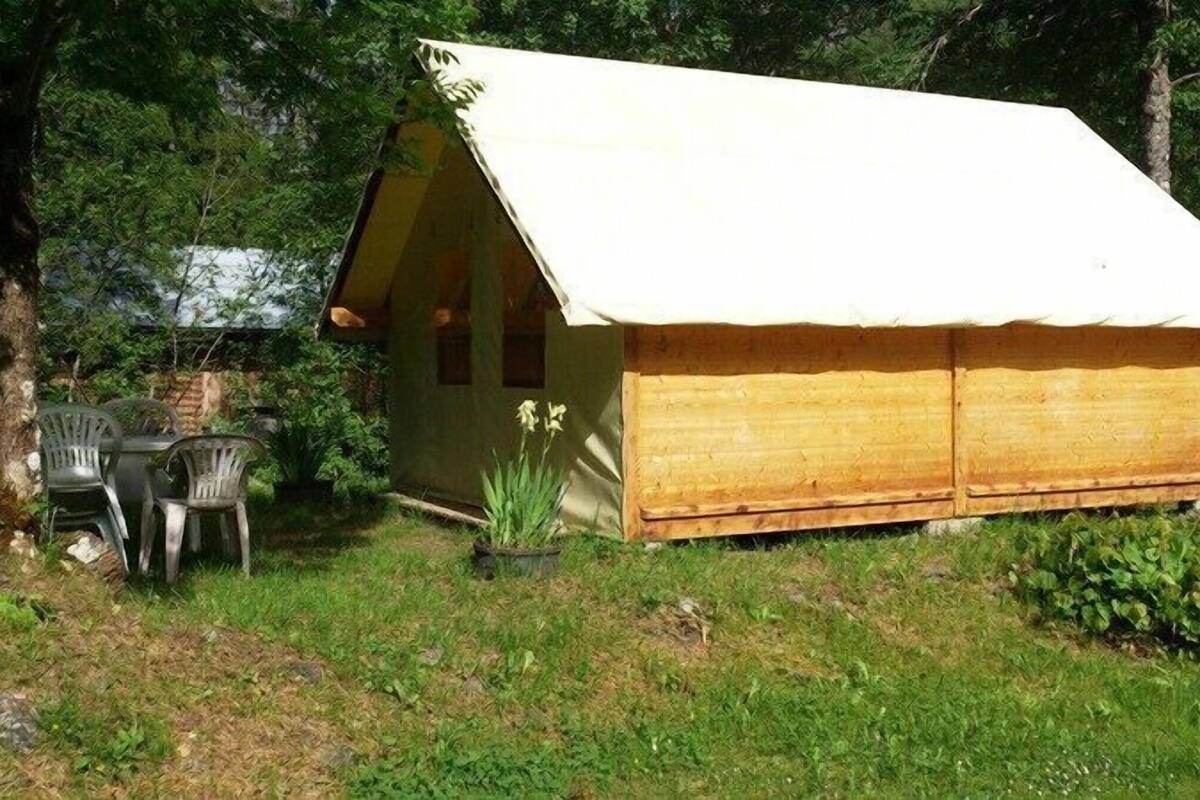 Une petite cabane en bois, dotée d’un toit à deux versants et d’un auvent blanc, entourée d’arbres et d’herbe.