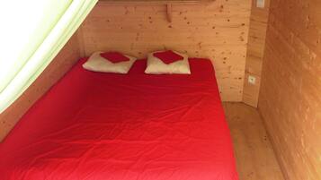 A small wooden cabin room with a single bed, two pillows, and a green curtain.