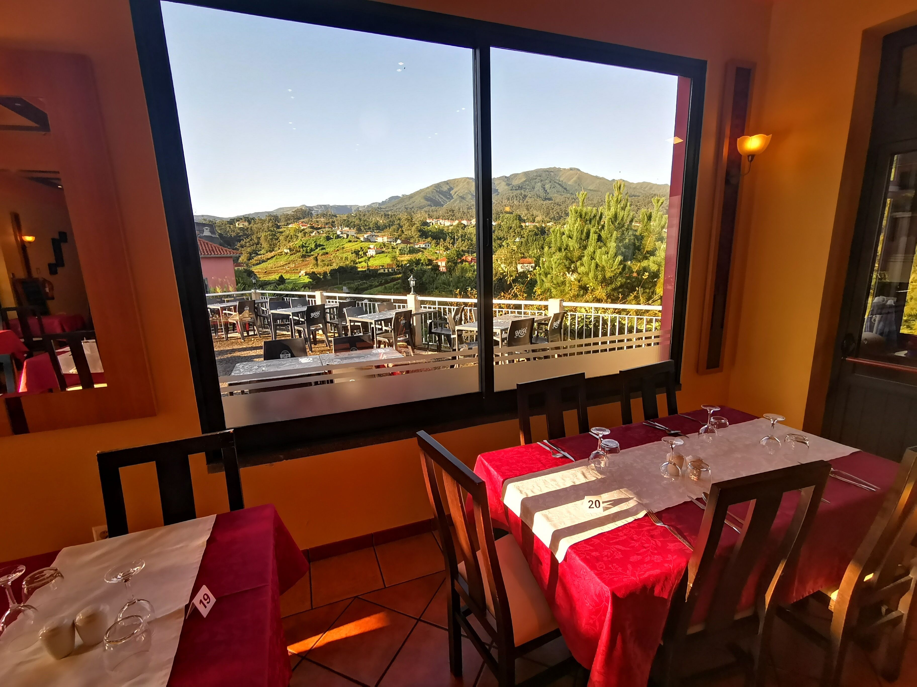 A dining area with tables set for two, a view of a mountainous landscape, and a terrace with outdoor seating.