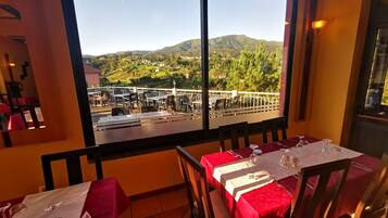 A dining area with tables set for two, a view of a mountainous landscape, and a terrace with outdoor seating.