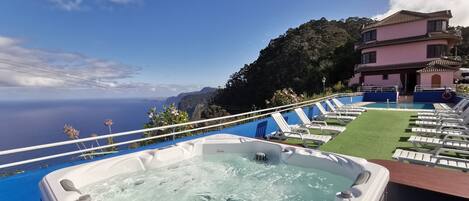 A hot tub with a view of the ocean and a building with a pink facade.