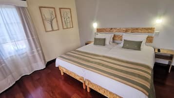 A bedroom with a wooden bed frame, a large bed with white bedding and green pillows, two wall-mounted picture frames, and a wooden nightstand with a lamp.