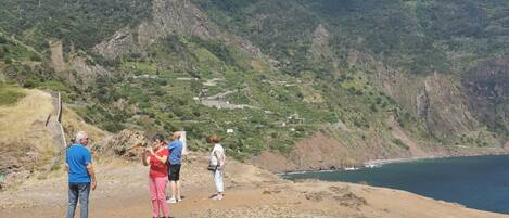 Un grupo de personas de pie en una ladera rocosa con vistas a una zona costera y montañas al fondo.