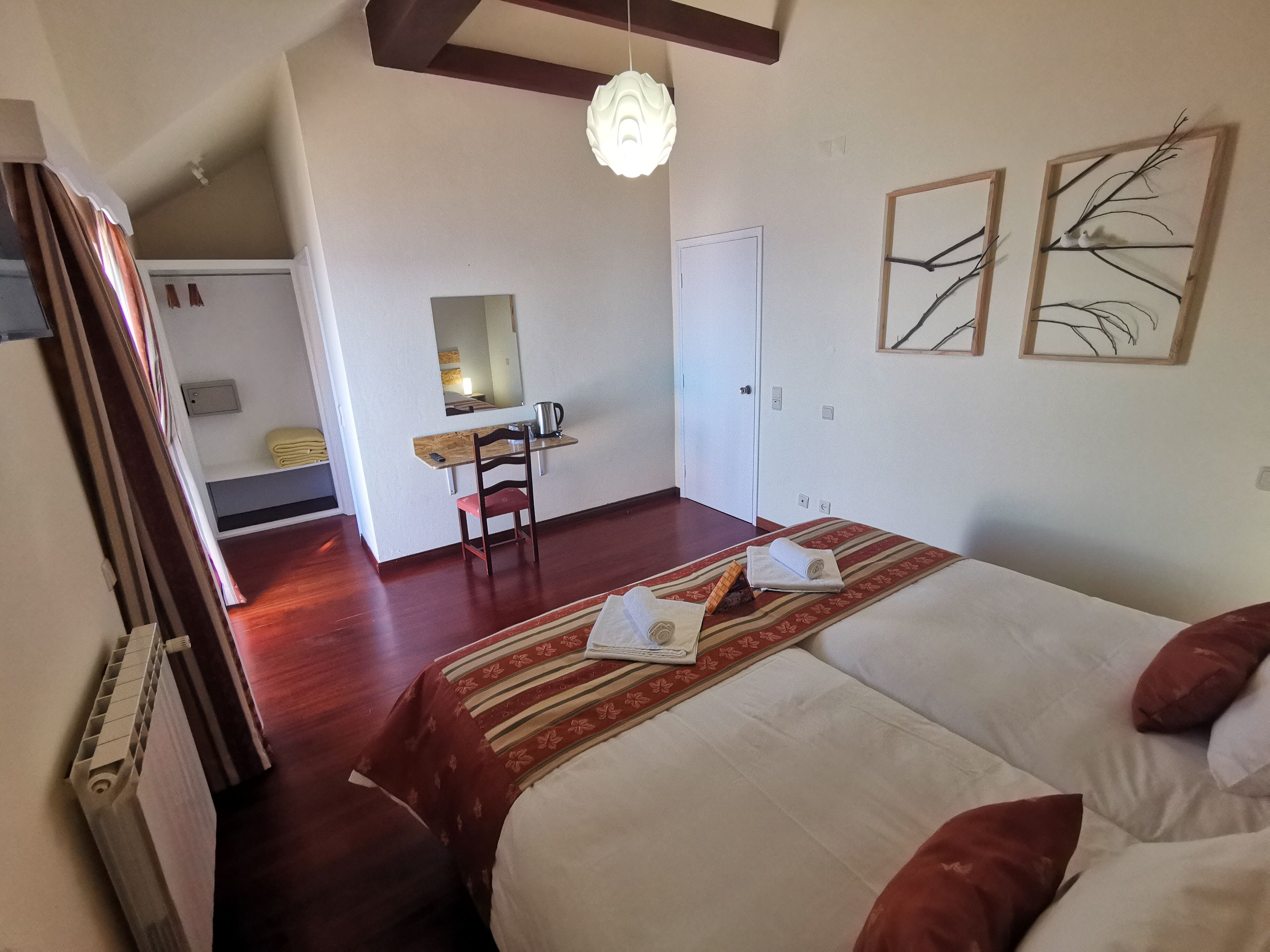 A hotel room with a bed, a desk, and a chair. There is a mirror on the wall and a window with curtains.