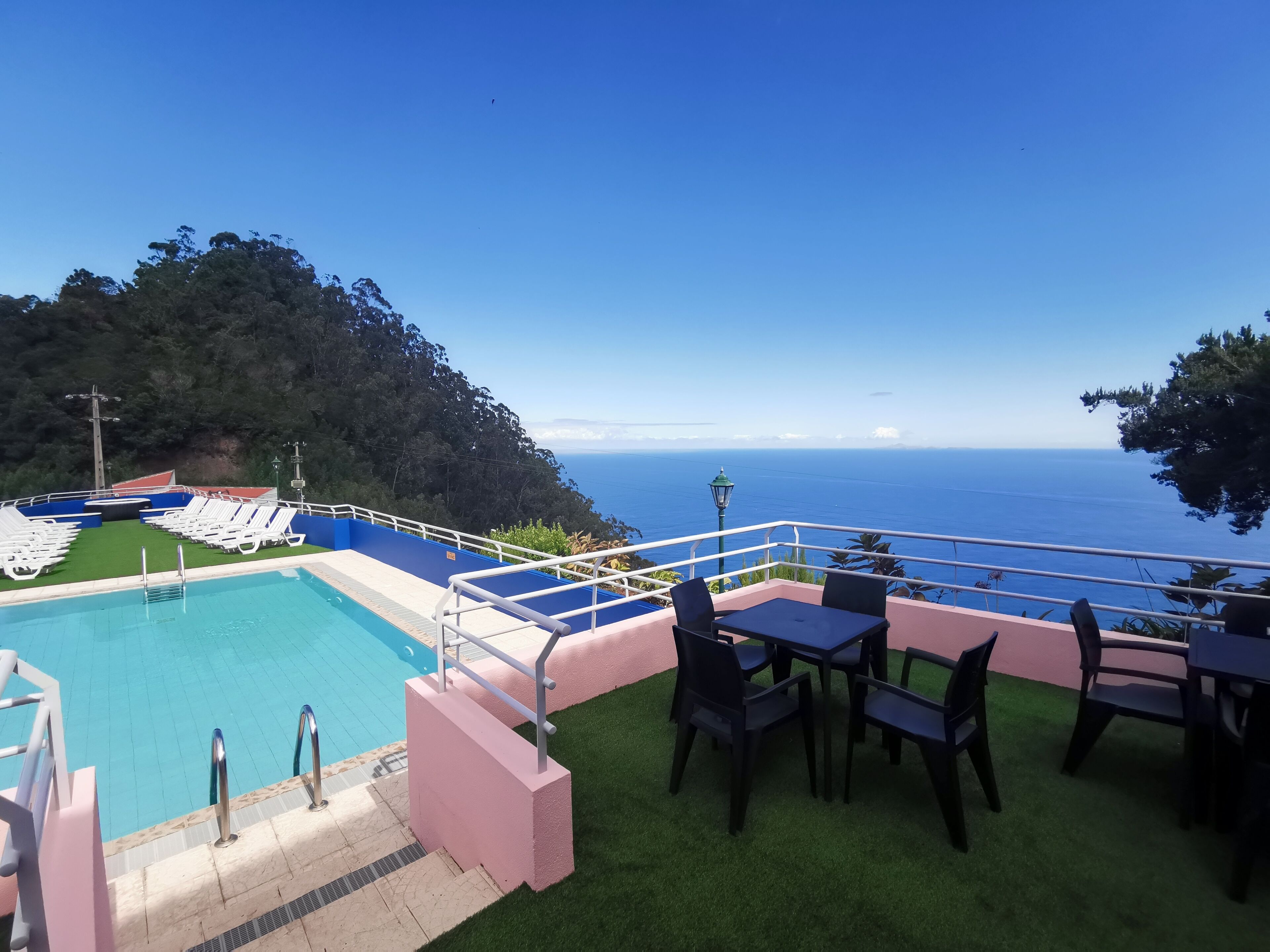 Zona de piscina con vista al océano, rodeada de vegetación y un espacio para comer.