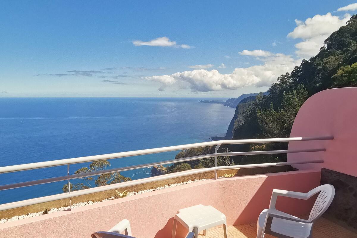 A balcony with a view of the sea and a pink wall.