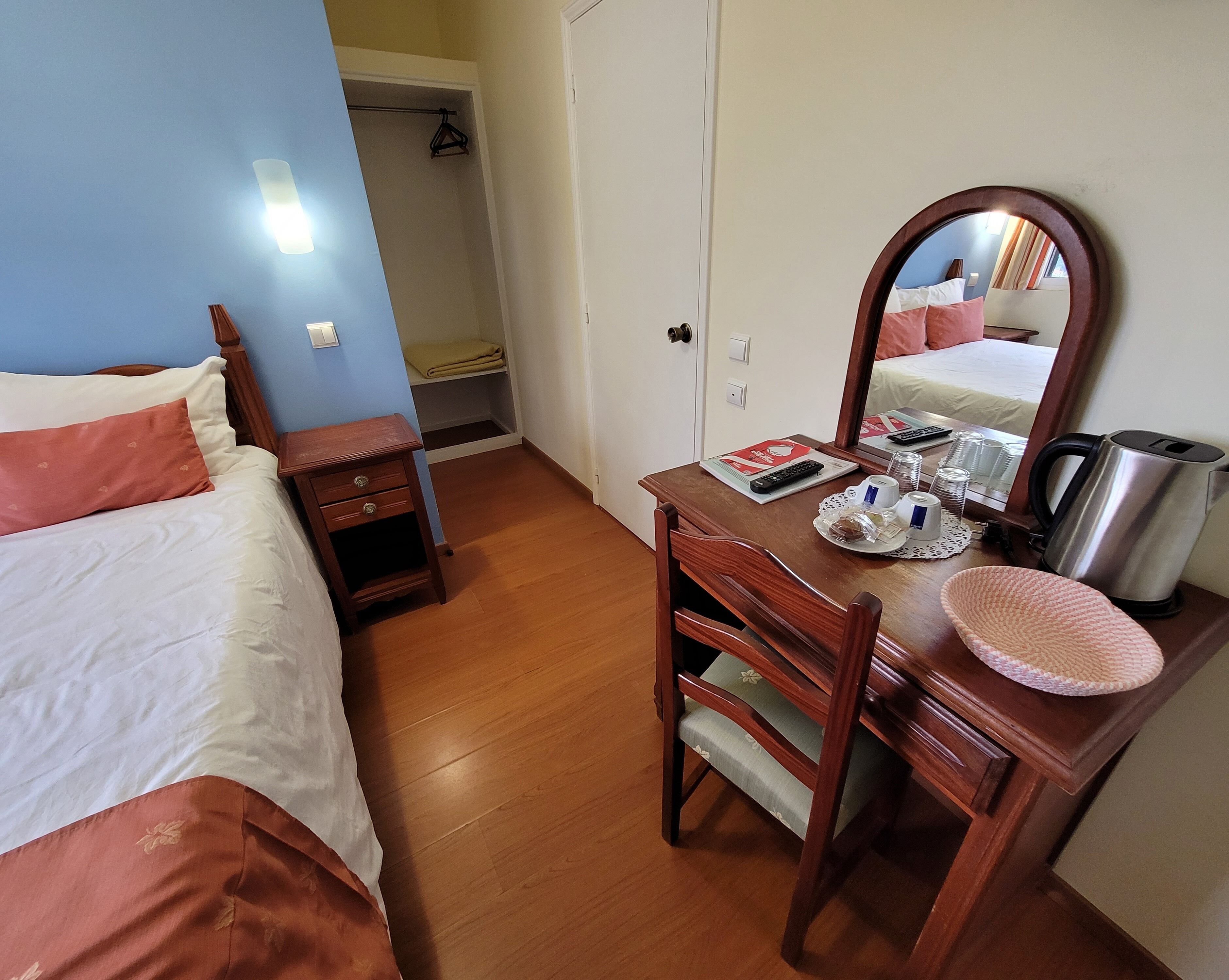 Ein Hotelzimmer mit Bett, Nachttisch aus Holz, Schreibtisch mit Stuhl, Spiegel und einer Küchenzeile.