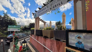 Señal de restaurante que indica 'Santana Nature Grill', con mesas al aire libre y un menú.