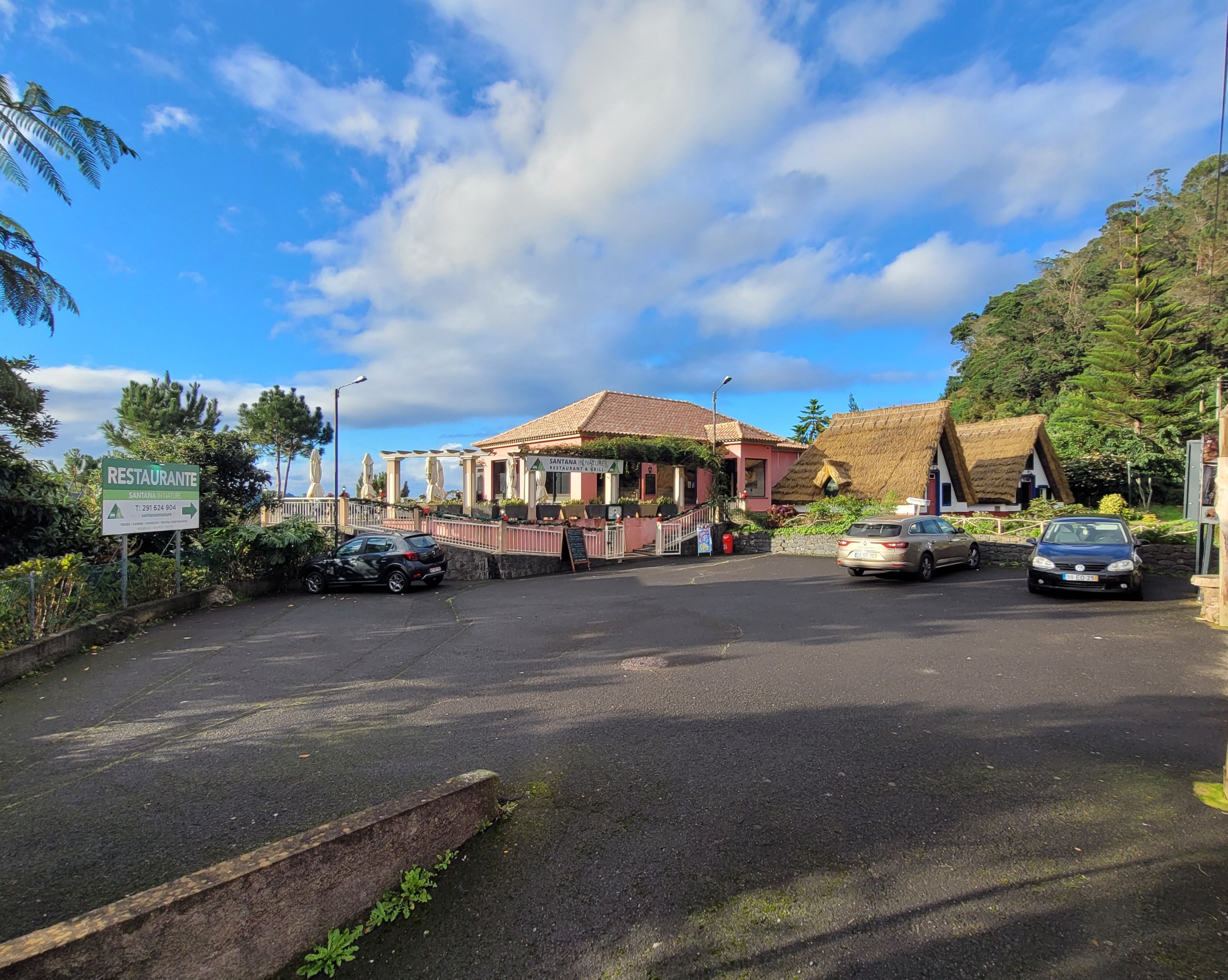 Un restaurant doté d’une terrasse, d’un bâtiment à toiture de chaume et de voitures garées à proximité.