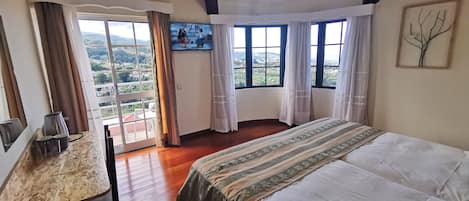 A bedroom with a large bed, a desk, and a view of a mountainous landscape through the windows.