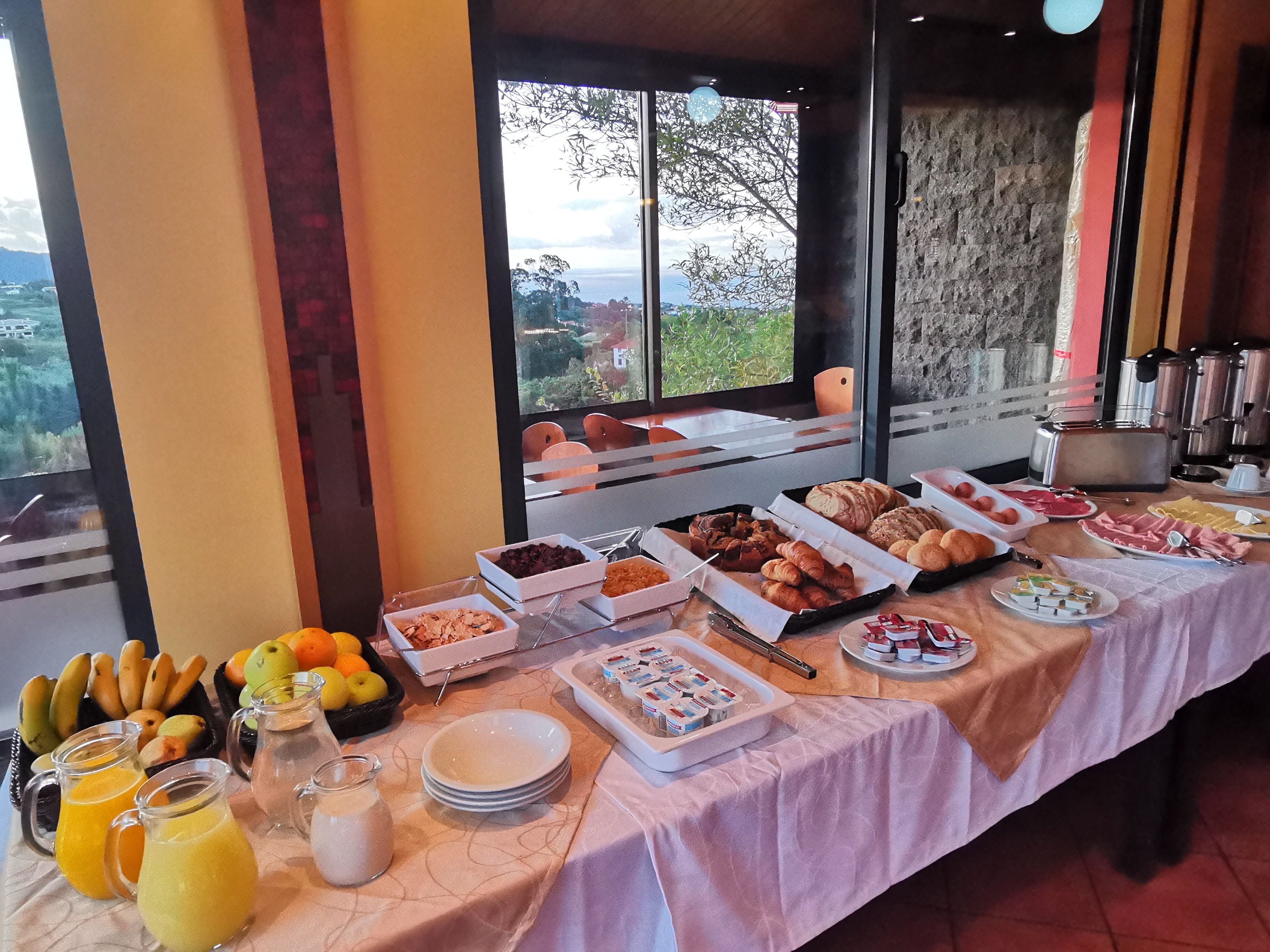 Un bufé de desayuno con diferentes alimentos y bebidas, con vistas panorámicas a través de amplios ventanales.