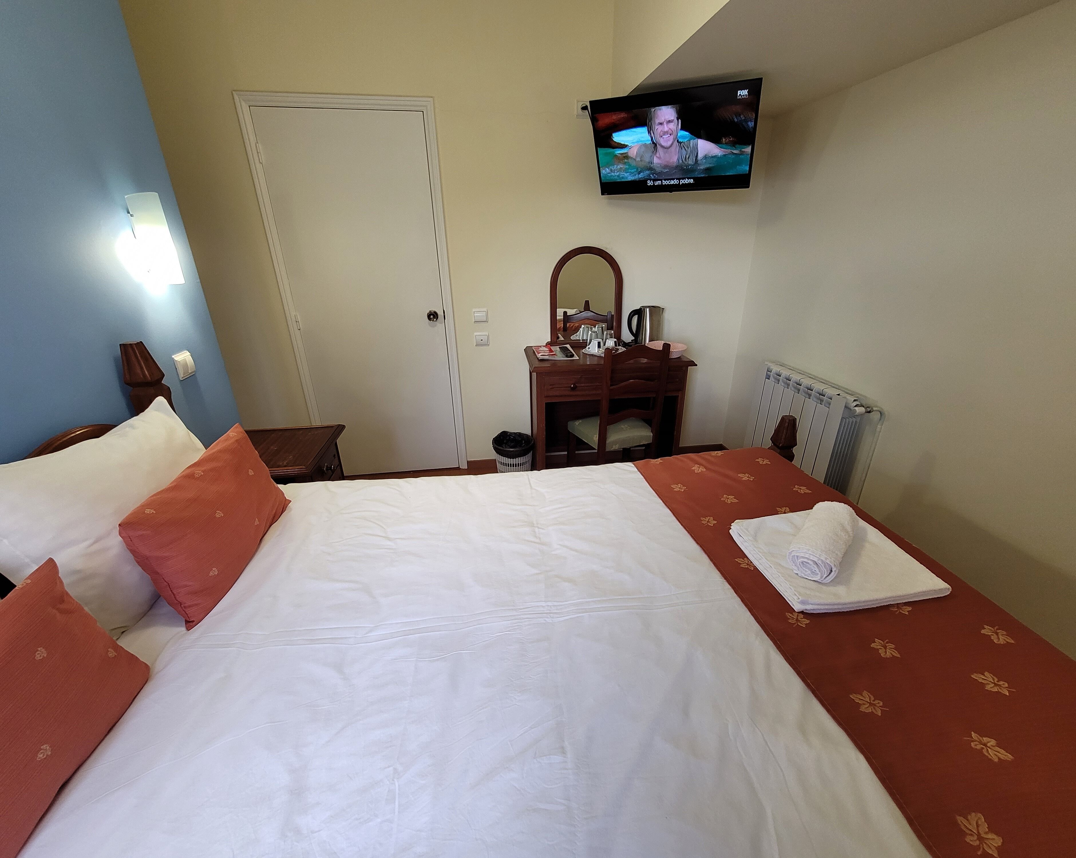 Una habitación de hotel con cama, escritorio, silla, televisor y radiador.