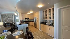 A modern kitchen with a central island, stainless steel appliances, and a dining area with a table set for four. - Sandbridge Beach Condo with fantastic Ocean View and Bay View Balcony!  (Virginia Beach)
