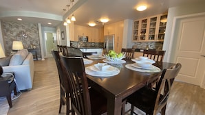 A dining area with a wooden table set for six, surrounded by chairs. There is a kitchen in the background with wooden cabinets and a microwave. - Sandbridge Beach Condo with fantastic Ocean View and Bay View Balcony!  (Virginia Beach)