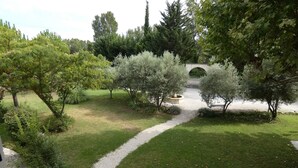A garden with a gravel path, trees, and a stone bridge. - Charming cottage in guest house on 6700m2 property, swimming pool, large garden (L'Isle-sur-la-Sorgue)