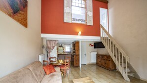 A living room with a sofa, a wooden coffee table, a dining table with chairs, a kitchen area, and a staircase. - Charming cottage in guest house on 6700m2 property, swimming pool, large garden (L'Isle-sur-la-Sorgue)