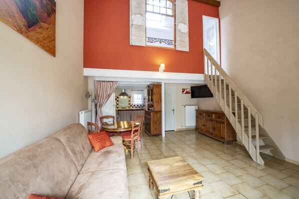 Un salon comprenant un canapé, une table basse en bois, une table à manger avec des chaises, un coin cuisine et un escalier.
