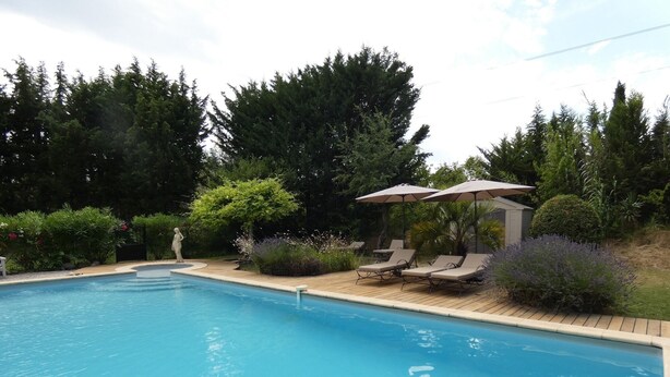 A swimming pool with lounge chairs and umbrellas, surrounded by greenery. - Charming cottage in guest house on 6700m2 property, swimming pool, large garden (L'Isle-sur-la-Sorgue)