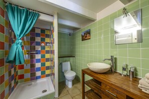 Une salle de bain avec un mur recouvert de carreaux colorés, des toilettes blanches, une baignoire et un meuble-lavabo en bois avec un évier.